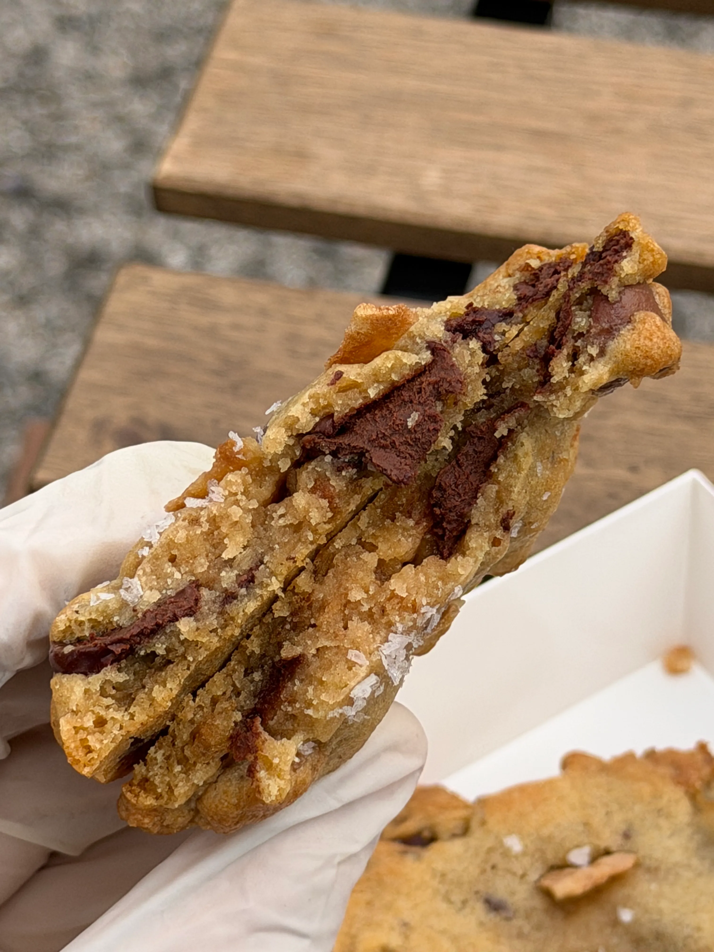 Gloved hand holding a thick cookie cross-section with visible chocolate filling.