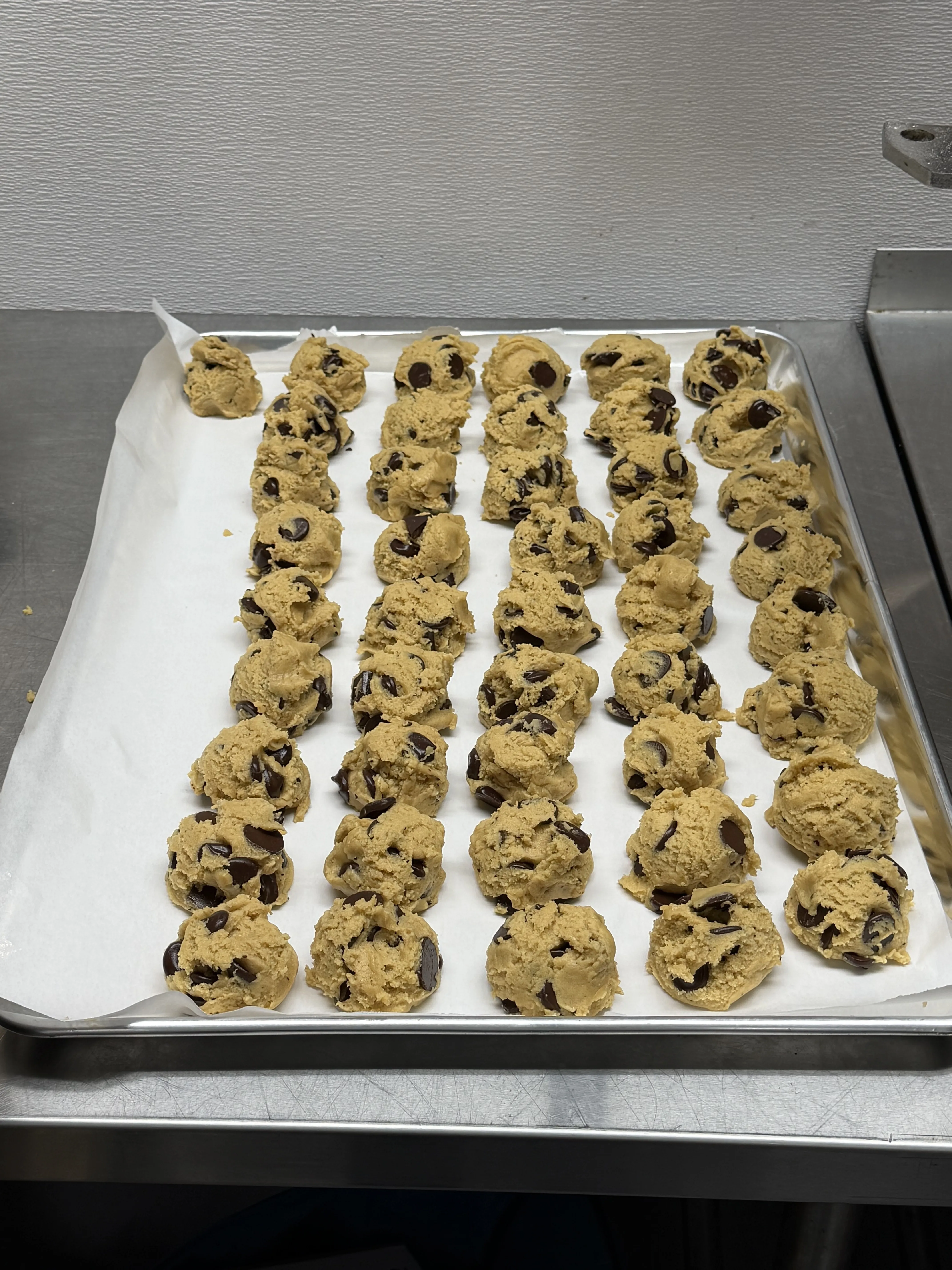 Sheet tray lined with neat rows of chocolate chip cookie dough in the bakery kitchen.