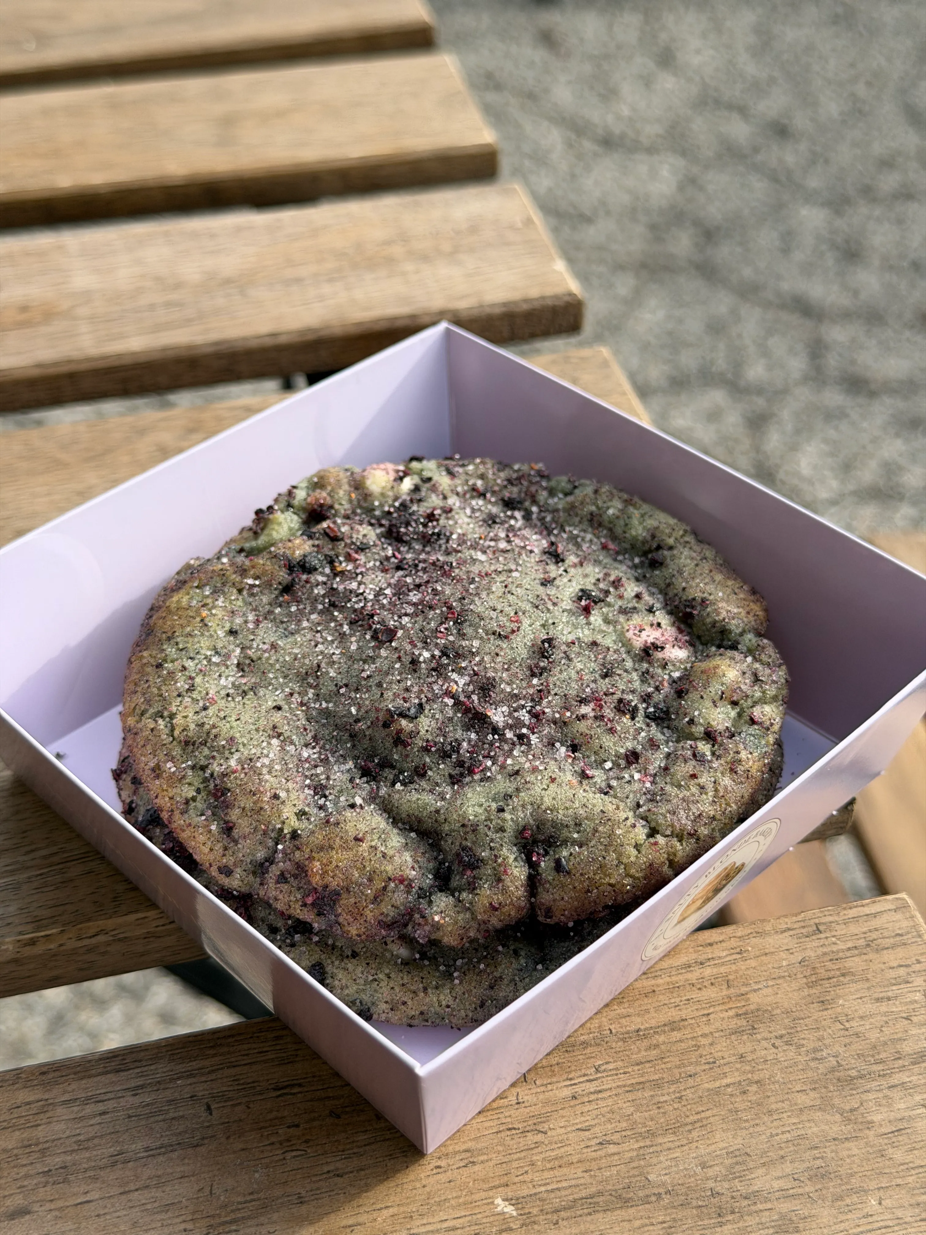 Dark cookies-and-cream style cookie resting in a lavender bakery box.