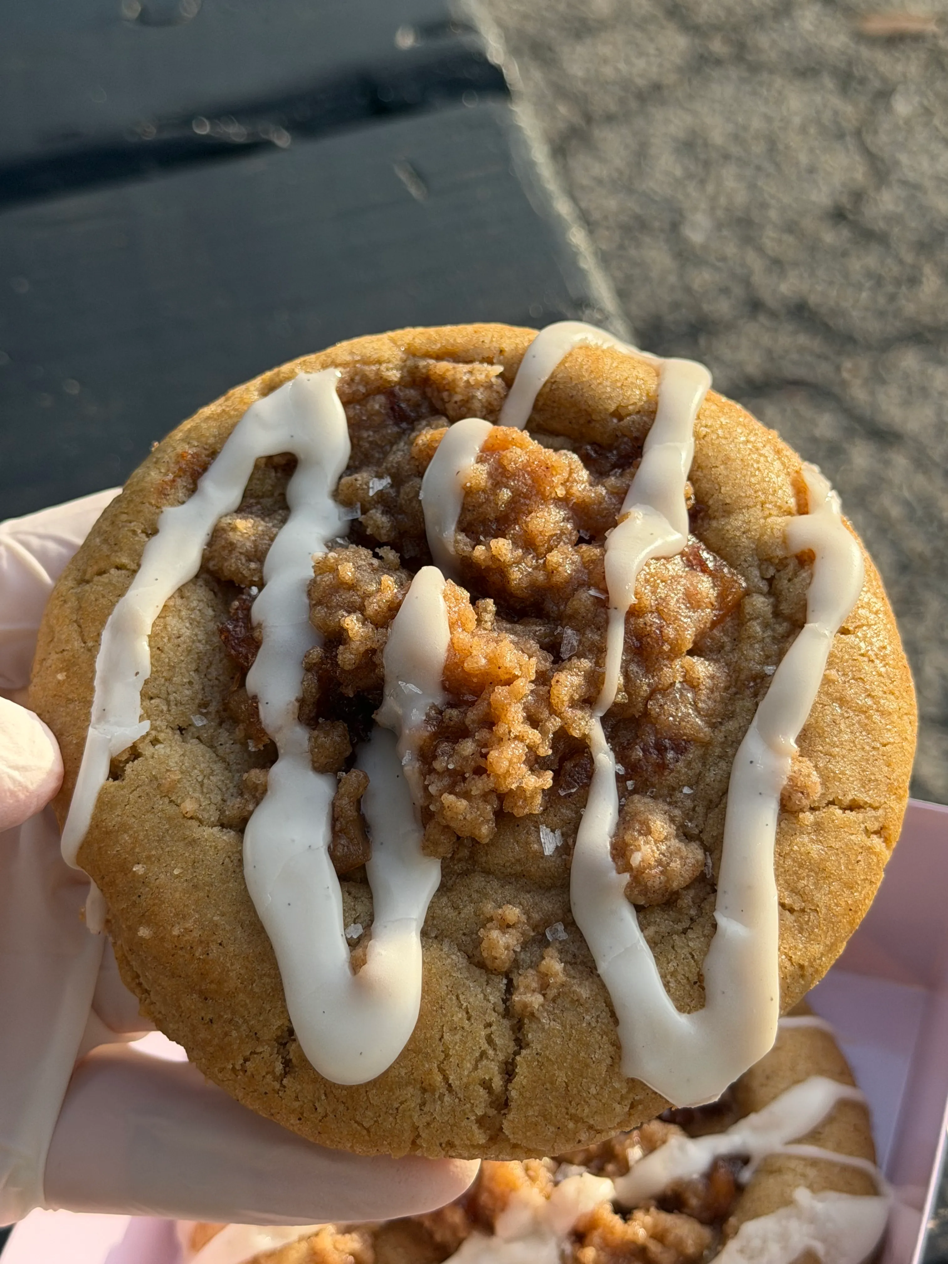 Thick cookie topped with icing and crumb pieces held close to the camera.
