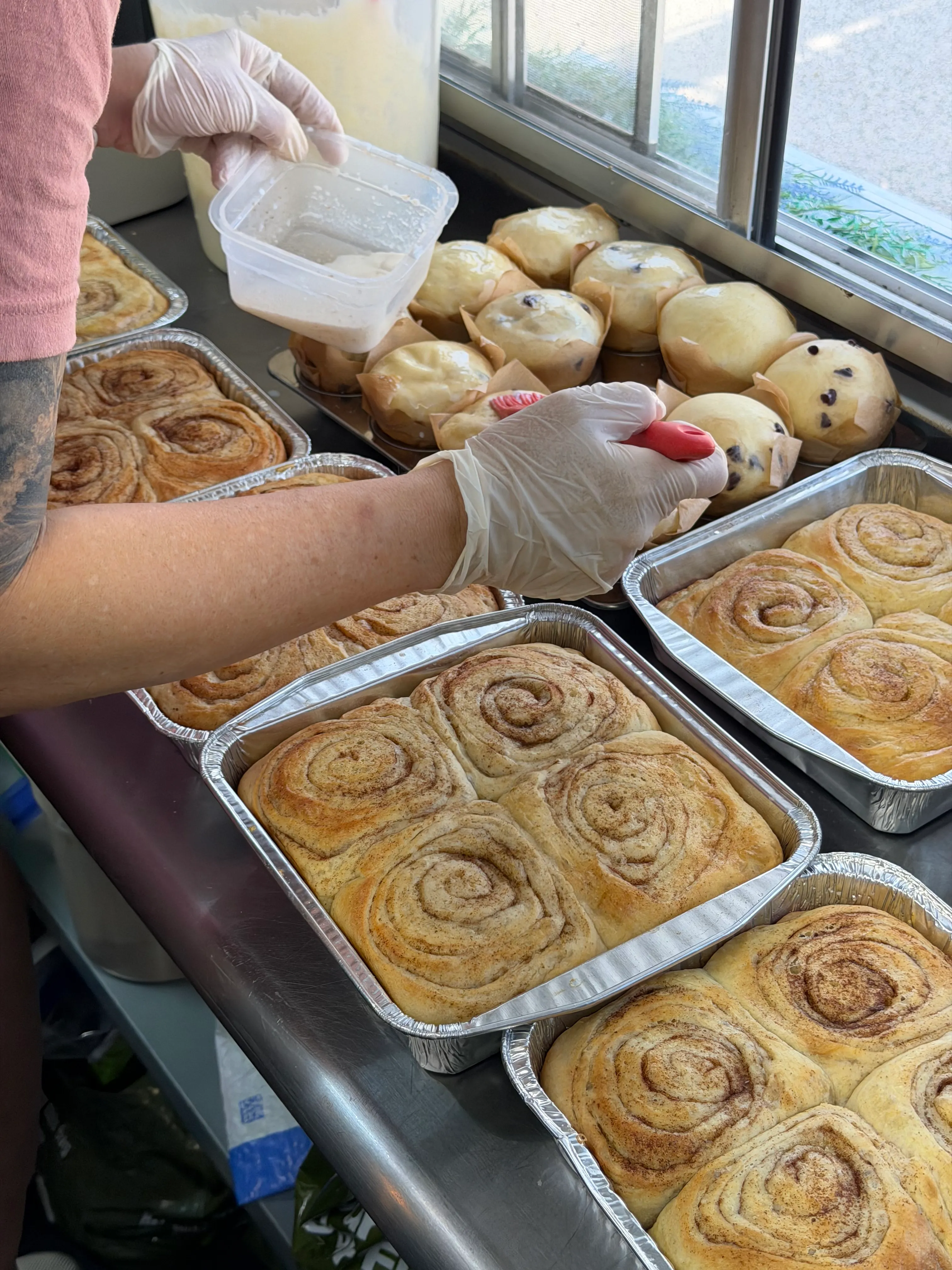 Baker working beside trays filled with rolls and other baked goods.